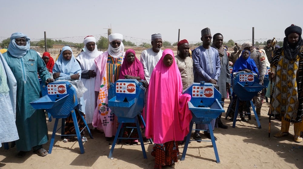 Teenage girls and men from Niger are standing next to grinding mills. 