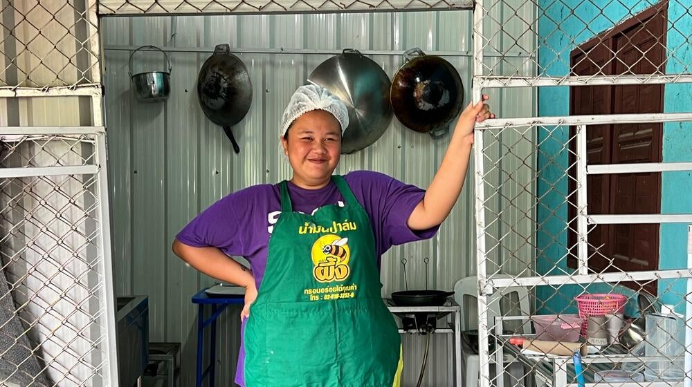 Une femme portant un tablier vert se tient dans une cuisine où Dok Jok est préparé.