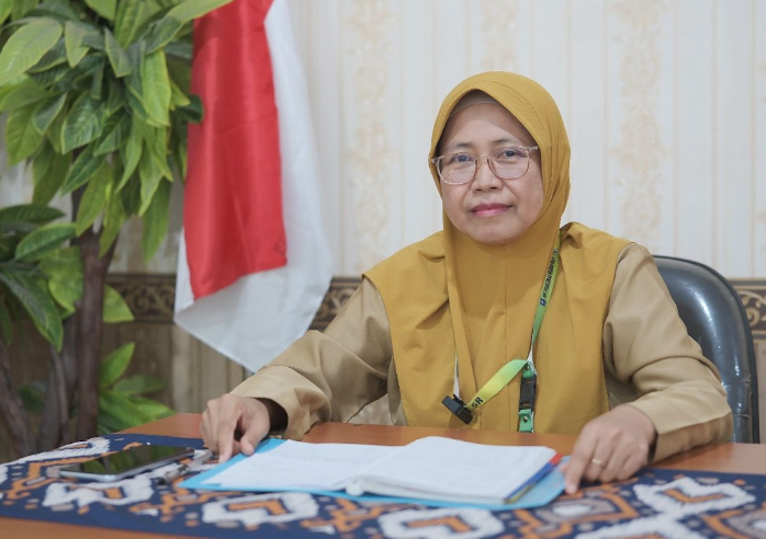 A woman in a yellow head covering sits behind a desk, with an open file in front of her