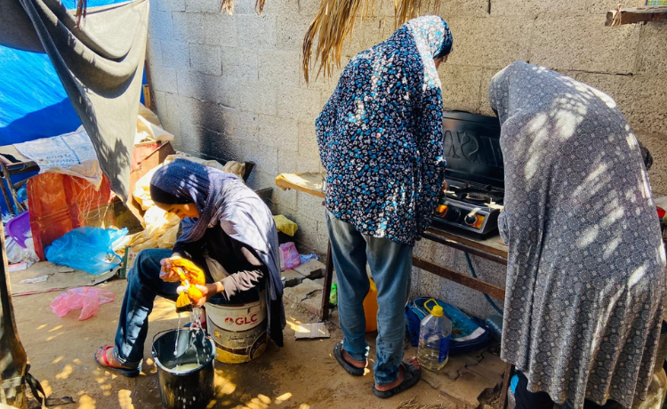 Trois filles s’affairent à cuisiner et nettoyer à l’extérieur d’une tente ouverte]