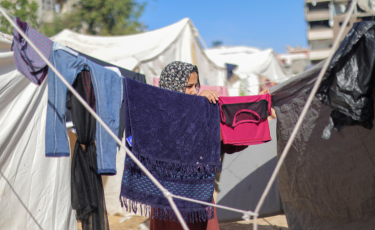 Une jeune fille étend du linge sur des cordes suspendues entre des tentes