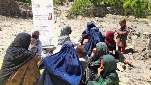 A group of women and children sit talking outside on rocky ground