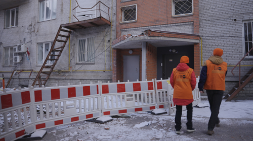 Dos personas con chalecos y gorras naranjas del UNFPA caminan hacia un edificio gravemente dañado