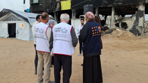 Un grupo de trabajadores sanitarios y personal del UNFPA frente a un gran edificio destruido y junto a una tienda médica con el logotipo del UNFPA