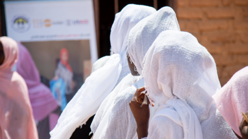 Mujeres con pañuelos blancos en la cabeza miran hacia un gran cartel con una mujer y un logotipo del UNFPA