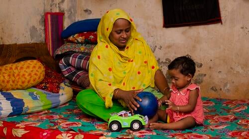 A mother plays with her child while sitting on a bed.