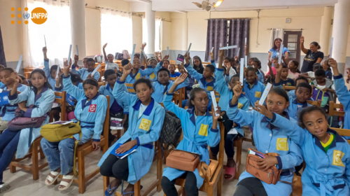 Un grupo de estudiantes con uniformes azules levantan las manos en un aula